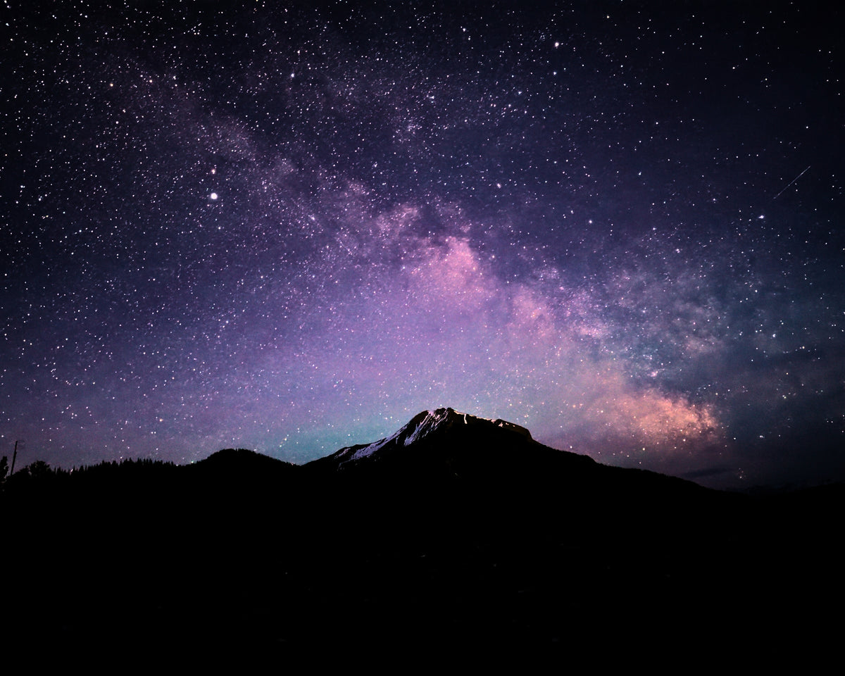 A star-filled night sky with the Milky Way stretching diagonally across a dark mountain silhouette.
