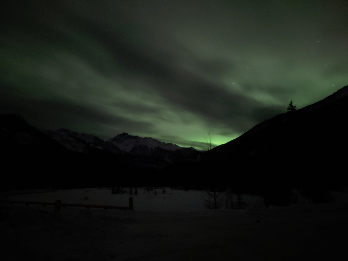 The first faint green glow of the aurora above a mountain ridge